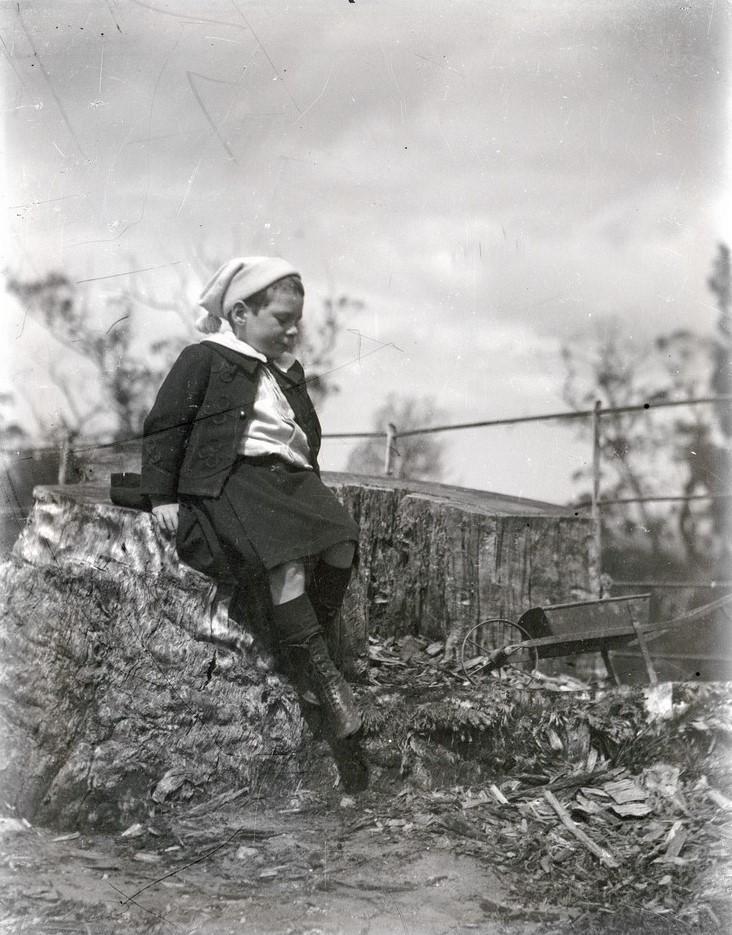 Young William Brooker in garden, with child-sized wheelbarrow in background