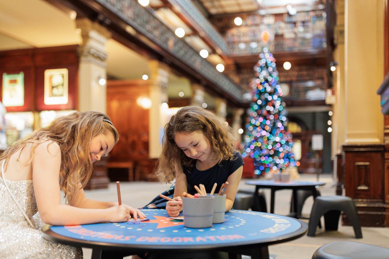 Two young girls colouring in with a Christmas tree in the background