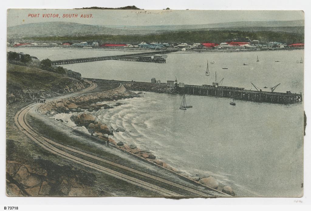 A colourised postcard showing the causeway, jetty and town buildings across the water. Photo taken from Granite Island at Port Victor in South Australia. SLSA: B 73718  