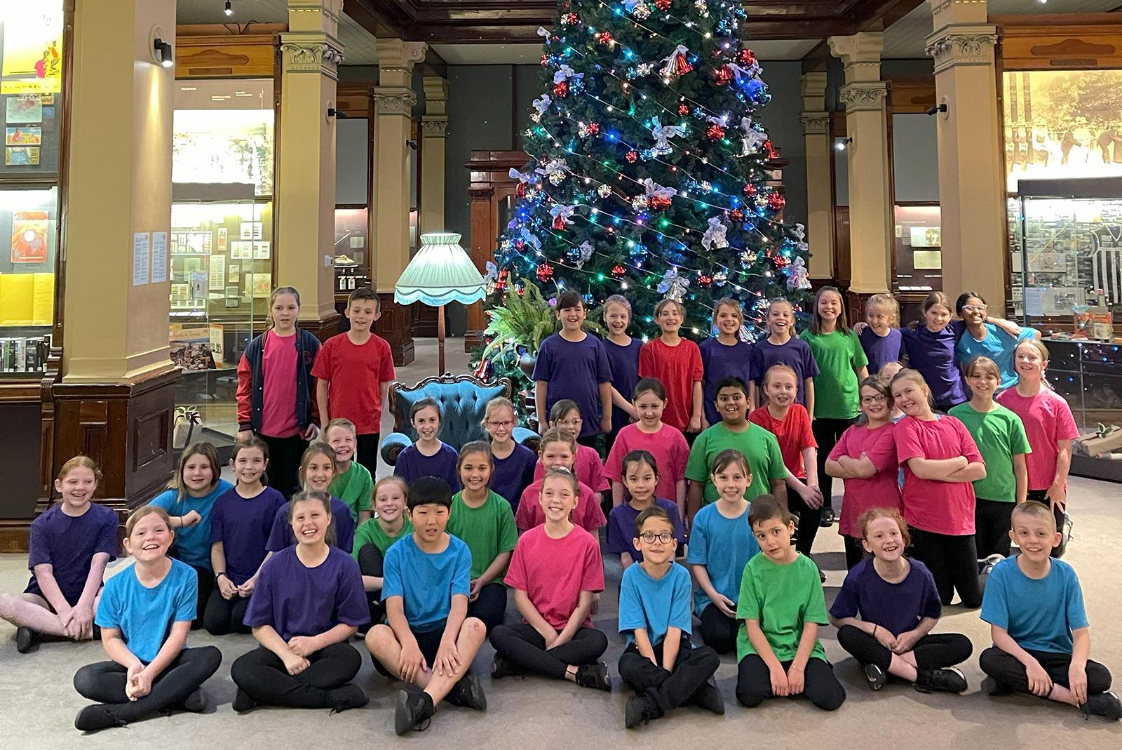 School choir singing in front of a Christmas tree.