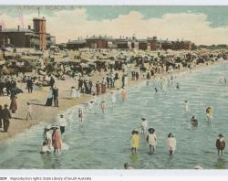 A postcard showing crowds of people at Glenelg Beach, in and out of the water, approximately 1900-1910. SLSA: B 77156/102/R      