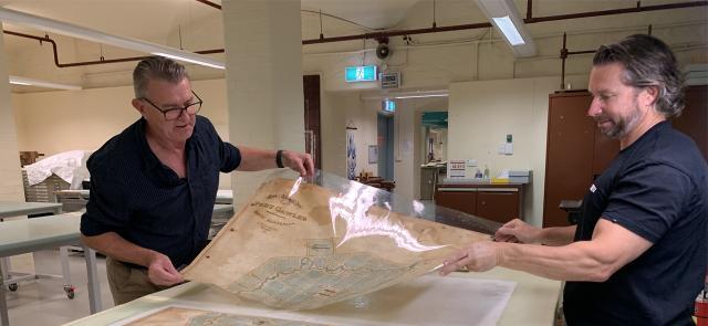 Two men carefully holding an old map during preservation work