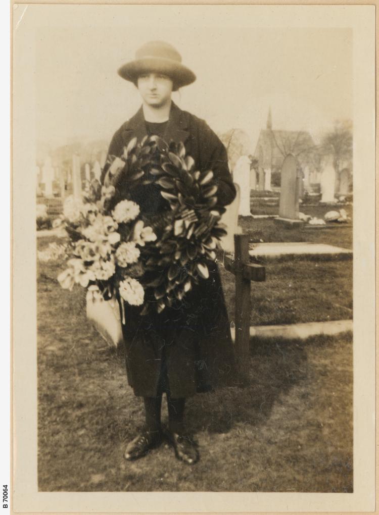 Young woman in England holding wreath of leaves and flowers to place on grave of Sapper AN Shuttleworth, UK, 1918